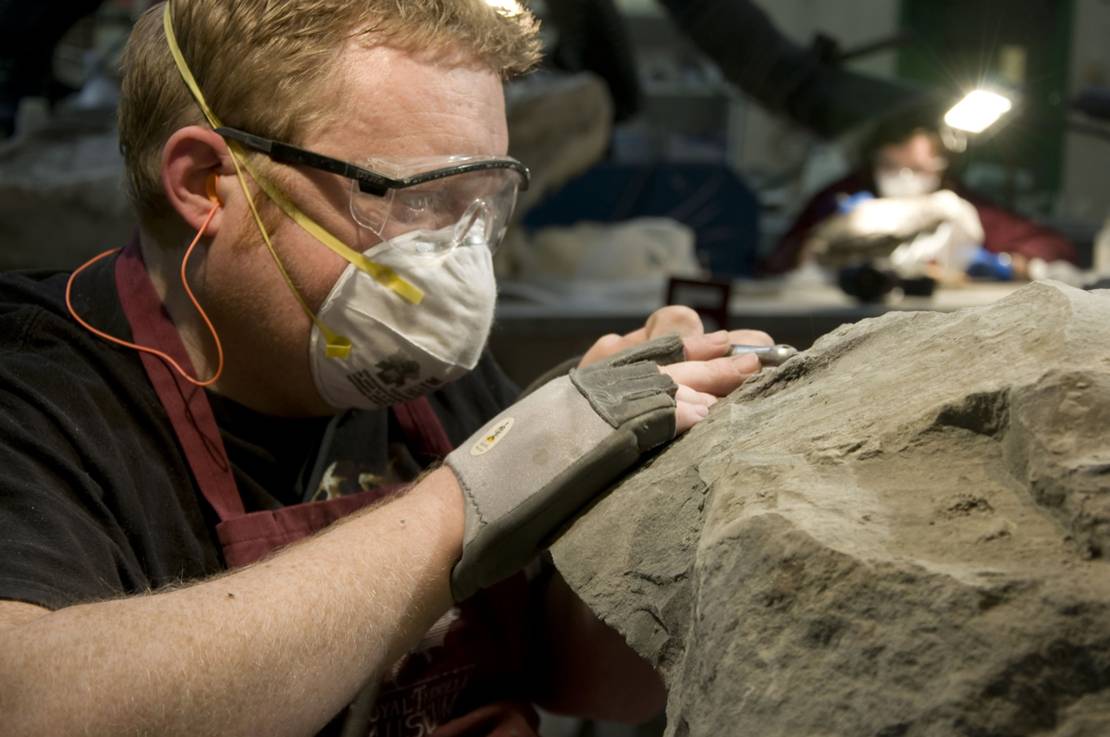 Mark Mitchell mit Mundschutz und Schutzbrille, der einen Stein bearbeitet.