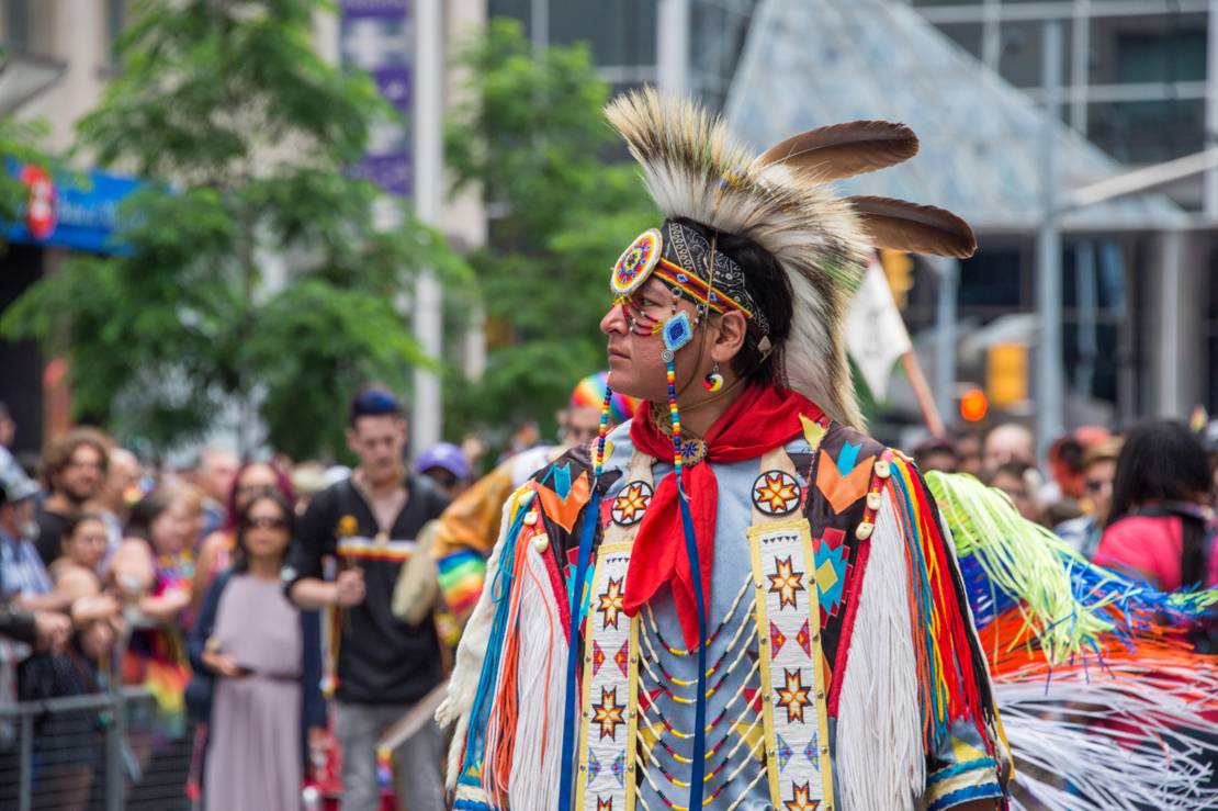 Ein Indianer steht in seinem traditionellen Gewand vor einer Gruppe Menschen.